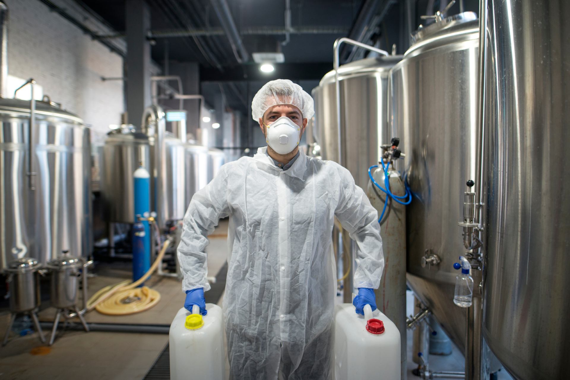 Industrial worker holding plastic cans with chemicals in production plant. Technologist wearing protection white uniform handling with aggressive chemicals substances.