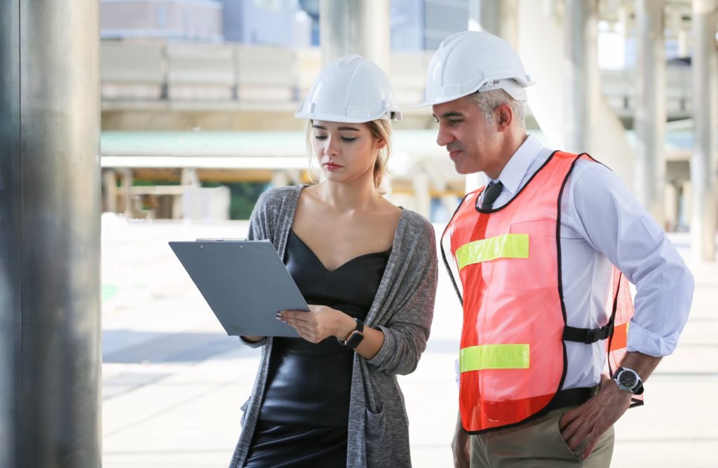 Female industrial engineer wearing a white helmet while standing in a construction site with businessman talking on working plan, Engineer and architects at construction site concept