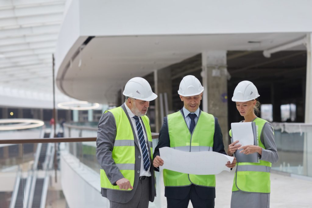 Ite Management Safety Training Scheme Officers Portrait of three successful business people wearing hardhats and inspecting plans while standing at construction site indoors, copy space