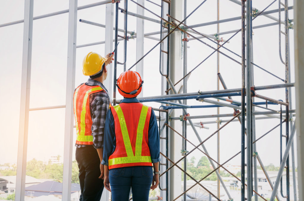 couple of engineer or technician man and woman with safety helmet holding mobile radio phone planning about building plan to greeting start up project in construction site building, industry concept