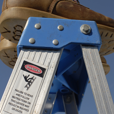 Person standing on top of a ladder, a sign showing ladder safety covering In House Courses